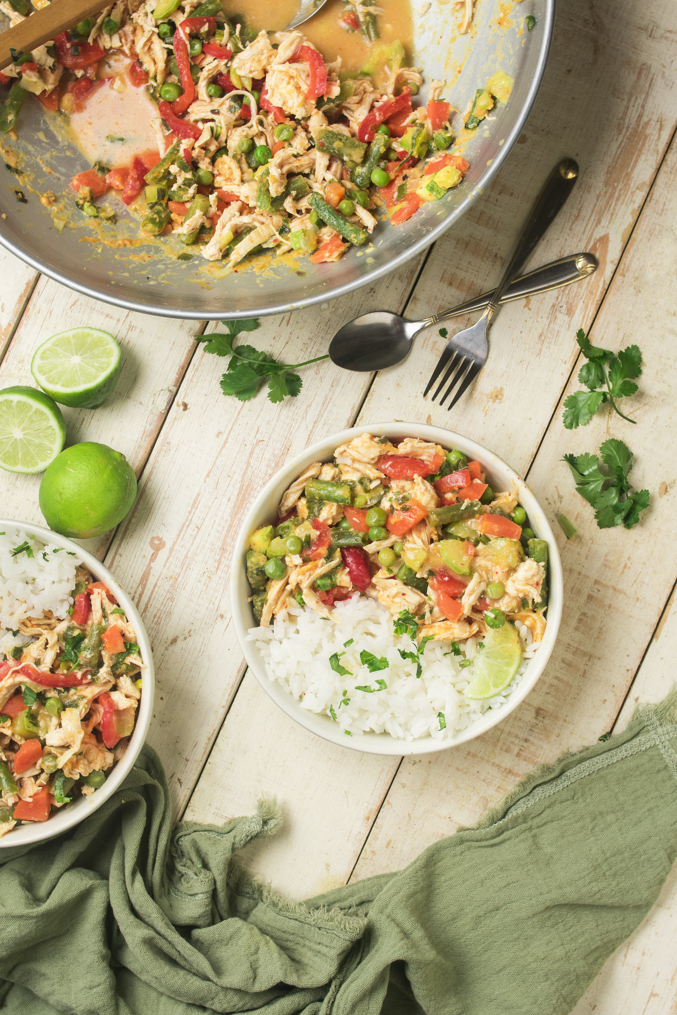Bowls of Thai-inspired chicken curry with jasmine rice, lime and coriander beside the wok.